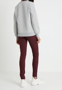 Grijze sweatshirt met lange mouwen, gecombineerd met strakke bordeauxrode broek en witte chunky sneakers, gezien vanuit de achterkant.