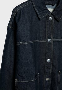 Denim jakna u tamnoplavoj boji s kontrastnim žutim šavovima, sa šiljastim ovratnikom, srebrnim dugmadima na pritisak i bočnim džepovima.