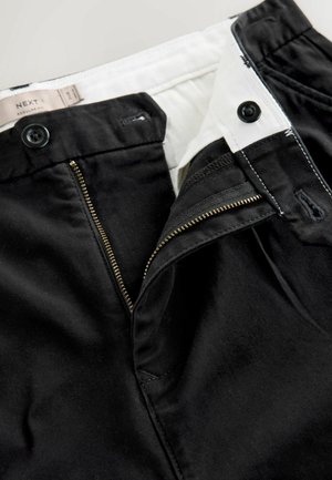Schwarze Hose mit Reißverschluss und goldfarbenem Metall-Reißverschluss, doppeltem Knopfverschluss und weißem Innenfutter, das eine glatte Stoffoberfläche zeigt.