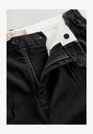 Mustad püksid, mis sisaldavad kuldse metallist lukuga, topeltnupuga kinnitust ja valget sisepinda, demonstreerides sujuvat kangasteksti.