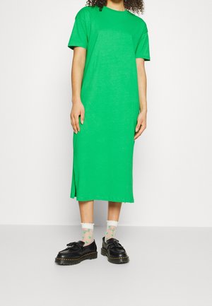 Person iført en lys grøn midi-kjole med korte ærmer, gennemsigtige hvide sokker med grønne print og sorte platformsko med kvaster.