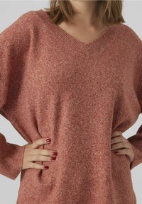 Sweter w serek, w oversize'owym kroju, wykonany z miękkiego, teksturowanego różowego materiału. Długie rękawy z prążkowanymi mankietami; ma mieszany, melanżowy wygląd.