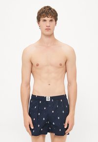 Marineblaue Badehosen aus leichtem Stoff, mit einem Muster aus kleinen, bunten Symbolen. Elastischer Bund mit einem zentralen Knopfdetail.