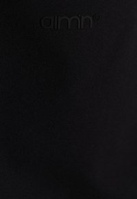 Melna apģērba auduma plāksne ar gludu tekstūru, kuras augšdaļā ir smalks reljefs ar logotipu "aimn®" atbilstošā krāsā.