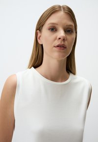 Witte mouwloze top met een ronde halslijn, gemaakt van gladde stof. Heeft een minimalistisch ontwerp zonder zichtbare patronen of accenten.