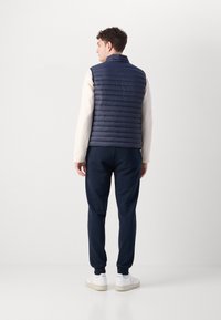 Vest puf din navy, cu cusături orizontale, purtat peste un hanorac de culoare crem. Asortat cu pantaloni închiși la culoare și adidași albi. Design simplu, fără logo-uri vizibile.