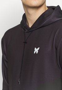 Felpa con cappuccio in tessuto viola scuro, dotata di un piccolo logo di una farfalla bianca sul petto e coulisse nere con punte in metallo.