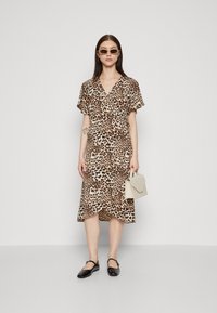 Robe portefeuille en imprimé léopard avec des manches courtes, décolleté en V et ourlet évasé. Associée à un sac à main de couleur claire et des ballerines noires.