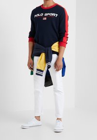 Navy sweatshirt with red accents and "POLO SPORT" logo, white pants, and white sneakers. Multi-colored jackets tied around waist.