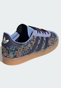 Sneaker con motivo floreale viola e accenti blu scuro, tre strisce più scure e suola in gomma traslucida. Presenta un morbido upper in tessuto.