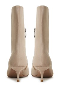 Beige suède enkellaarsjes met een spitse neus en een dunne hak. Achterzijdige ritssluiting en een gladde textuur, met zichtbare stikseldetails.