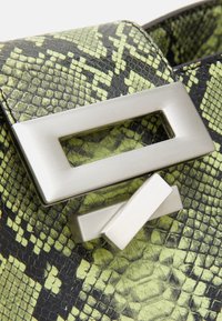 Sac texturé en peau de serpent verte et noire avec une grande fermeture métallique argentée rectangulaire.