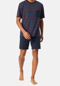 Navy plaid t-shirt with red and green accents, featuring a chest pocket, paired with solid navy shorts. Cotton blend, casual fit, short sleeves.