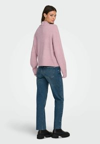 Lys rosa genser med ribbestrikket kant og perleaccenter på ermene, kombinert med blå rettkutt jeans og svarte chunky støvler.