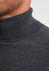 Suéter de cuello alto en gris oscuro con textura acanalada, diseño ajustado y un acabado suave, que enfatiza su material blando y estructura.