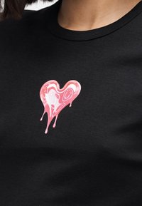 Camiseta de algodón negra con un gráfico de corazón rosa goteando en el pecho, con elementos de diseño texturizados y un escote redondo.