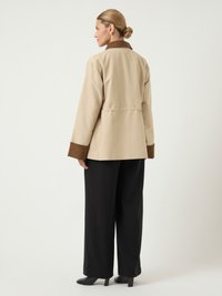 Μπεζ σακάκι με καφέ γιακά και μανσέτες, με χαλαρή σχεδίαση. Φοριέται με μαύρα παντελόνια φαρδιάς γραμμής και τακούνια.