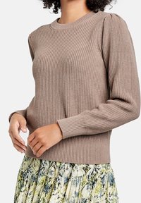 Lysbrun strikket sweater med ribbet tekstur, rund halsudskæring og ballonærmer, parret med en mønstret multi-farvet nederdel.