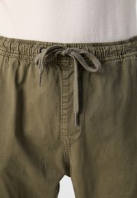 Khaki shorts met een elastische tailleband en trekkoord, voorzien van metalen toggles. Het materiaal is een zachte, gestructureerde stof met een relaxte pasvorm.