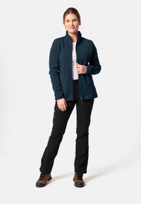 Marineblauer Fleece-Reißverschlussjacke mit hohem Kragen, kombiniert mit schwarzen Hosen. Die Jacke hat eine dezente Textur und einen Frontreißverschluss.