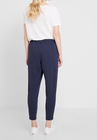 Marinblå joggers med avslappnad passform, elastisk midja och avkortade benslut, tillsammans med en vanlig vit t-shirt med kort ärm.