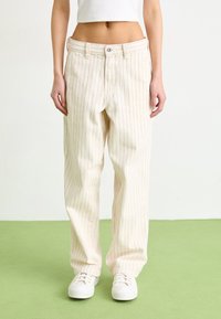 Cream-colored, wide-leg pants with red vertical stripes and a button closure. Worn with white sneakers. Smooth fabric, slightly textured.