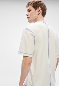 T-shirt branca de manga curta com costura contrastante azul ao longo das bordas e da costura traseira. Textura suave e macia, corte descontraído.