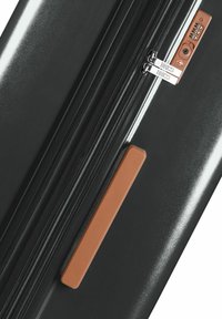 Valigia rigida nera con finitura testurizzata, dotata di maniglia in bronzo, doppia cerniera e lucchetto a combinazione. Design minimalista con linee pulite.