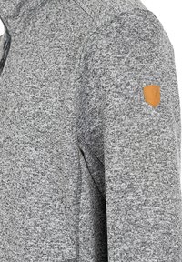 Grå texturerad hoodie med halvmatchning, med en liten badge i tan läder på axeln och fina sömnadsdetaljer.