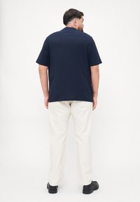Granatowy t-shirt z krótkim rękawem, luźny krój, w połączeniu z jasnymi spodniami o szerokich nogawkach i czarnym obuwiem, widok z tyłu.