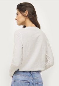 White long-sleeve shirt made of lightweight fabric. Simple round neckline, soft texture, and relaxed fit, paired with blue denim jeans.
