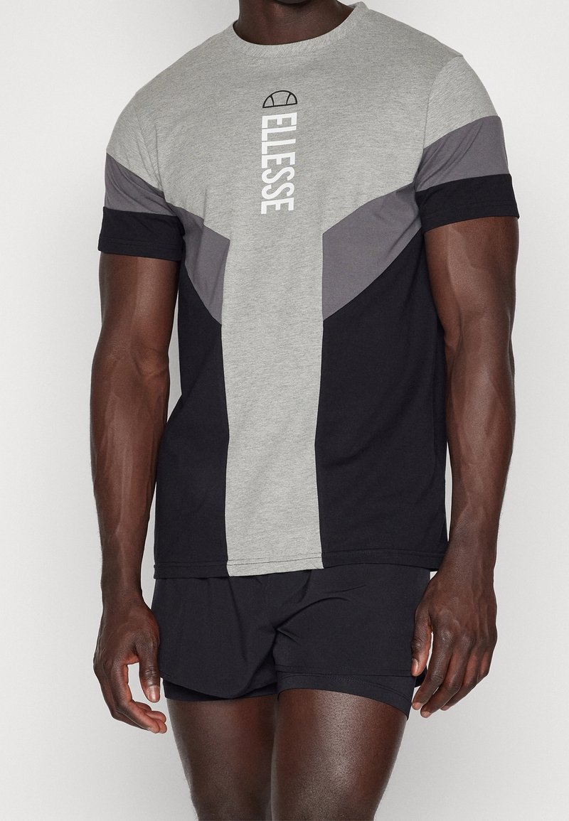 Grå och svart kortärmad t-shirt med geometrisk färgblockering, med en vit logotyp och rundad halsringning. Materialet verkar vara en bomullsblandning.