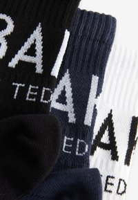 Kolme paria sukkia mustana, tummansinisenä ja valkoisena, joissa on rohkeaa "TED"-kirjoitusta. Materiaali näyttää neulotulta ja siinä on ribbitekstuuri.
