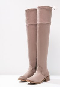 Beżowe kozaki do kolan z ekologicznej zamszowej skóry, na obcasie typu bloczek, z bocznym zamkiem i zaokrąglonym noskiem. Charakteryzują się gładką fakturą i prostym designem.