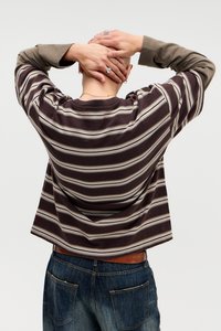 Camisa de mangas longas às riscas em castanho escuro e bege, com um corte descontraído, apresentando mangas largas. Combinada com jeans de denim azul em estilo de cintura média.