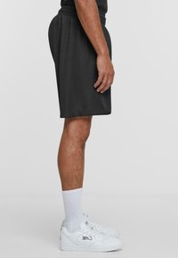 Sorte treningsshorts laget av pustende mesh, med elastisk liv. Kombinert med hvite joggesko og ribbede hvite sokker.