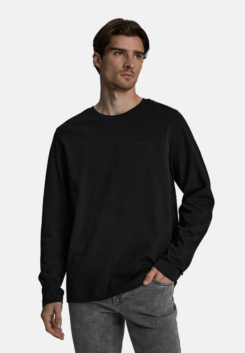 Czarna longsleeve z dzianiny, z okrągłym dekoltem i subtelnym logo na piersi, w połączeniu z szarymi dżinsami.