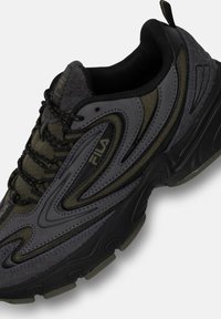 Scarpa sportiva grigio scuro con tomaia testurizzata e accenti neri e oliva, suola ammortizzata e elementi di design ondulati a contrasto.