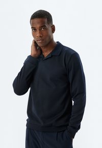 Dunkelblaues Langarm-Polohemd mit Kragen, gerippten Bündchen und Saum. Glatte Textur mit minimalen Nähdetails.