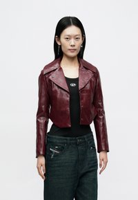 Bordeauxfarbige, kurze Lederjacke mit großen Revers, glänzender Textur und Druckknopfverschlüssen, kombiniert mit dunklen Denim-Jeans mit Used-Details.