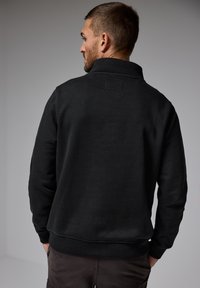 Svart fleece-tröja med hög krage, ribbade ärmslut och nederkant, med en slät textur och minimalistisk design.