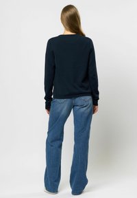 Hanorac bleu marin cu mâneci lungi și gât rotund, asortat cu blugi decolorati cu picior larg și detalii la buzunarele din spate.