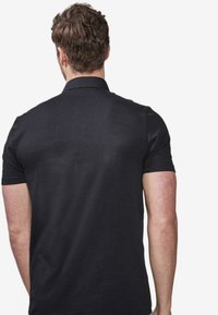 Sort polo skjorte med korte ærmer, en robust krave og en glat tekstur; passer tæt til skuldrene og snævrer ind mod taljen.