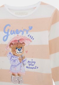 Camicia a maniche corte in cotone organico bianco con strisce pesca, con un orsetto cartoon che tiene un ombrello e la scritta "goditi il tuo momento".