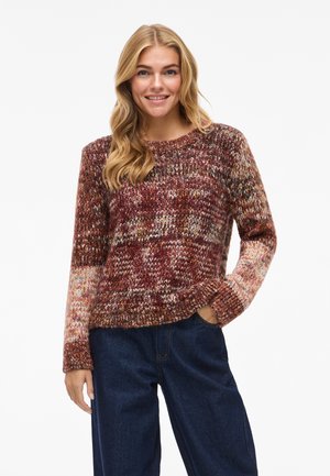 Knit sweater in warm tones of burgundy, orange, and cream. Features textured fabric, long sleeves, and a crew neckline. Paired with dark denim.