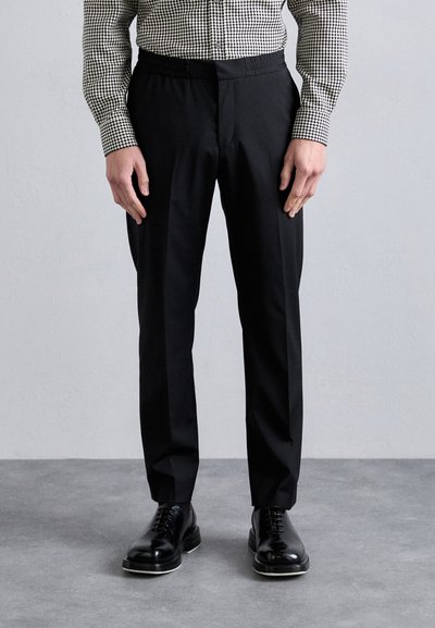 Pantaloni negri personalizați, cu un tiv elastic, având o textură netedă și un design ajustat. Asortați cu pantofi negri, lucioși, cu șireturi.