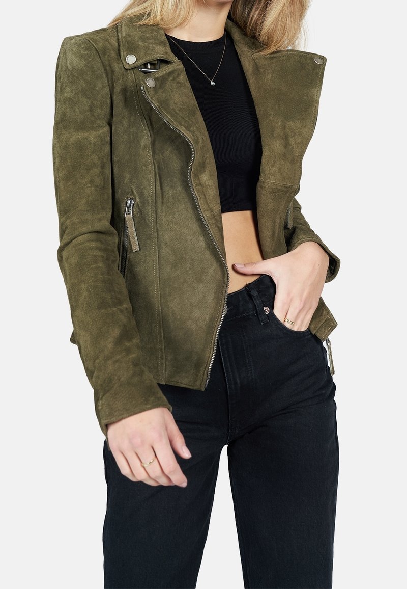 Olivgröna mockajacka med bikerstil, asymmetrisk dragkedja, tryckknappar på kragen och texturerade detaljer. Bärs över en svart crop top och byxor.