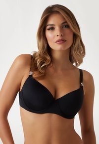 Zwarte onderwired bra van gladde stof, met gemodelleerde cups en verstelbare bandjes met decoratieve hardware accenten. Eenvoudig, slank ontwerp.