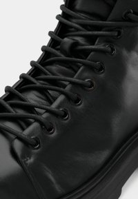 Botte noire en cuir avec des lacets ronds noirs passés à travers des œillets en métal, gros plan montrant la texture lisse et la semelle épaisse.