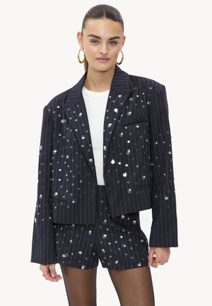 Conjunto de blazer y pantalones cortos de rayas negras, adornado con embellishments circulares reflectantes. La chaqueta cuenta con un cuello con muesca y un bolsillo frontal.